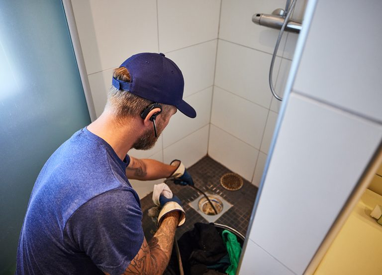 Man som utför högtrycksspolning i golvbrunn för att lösa upp ett stopp